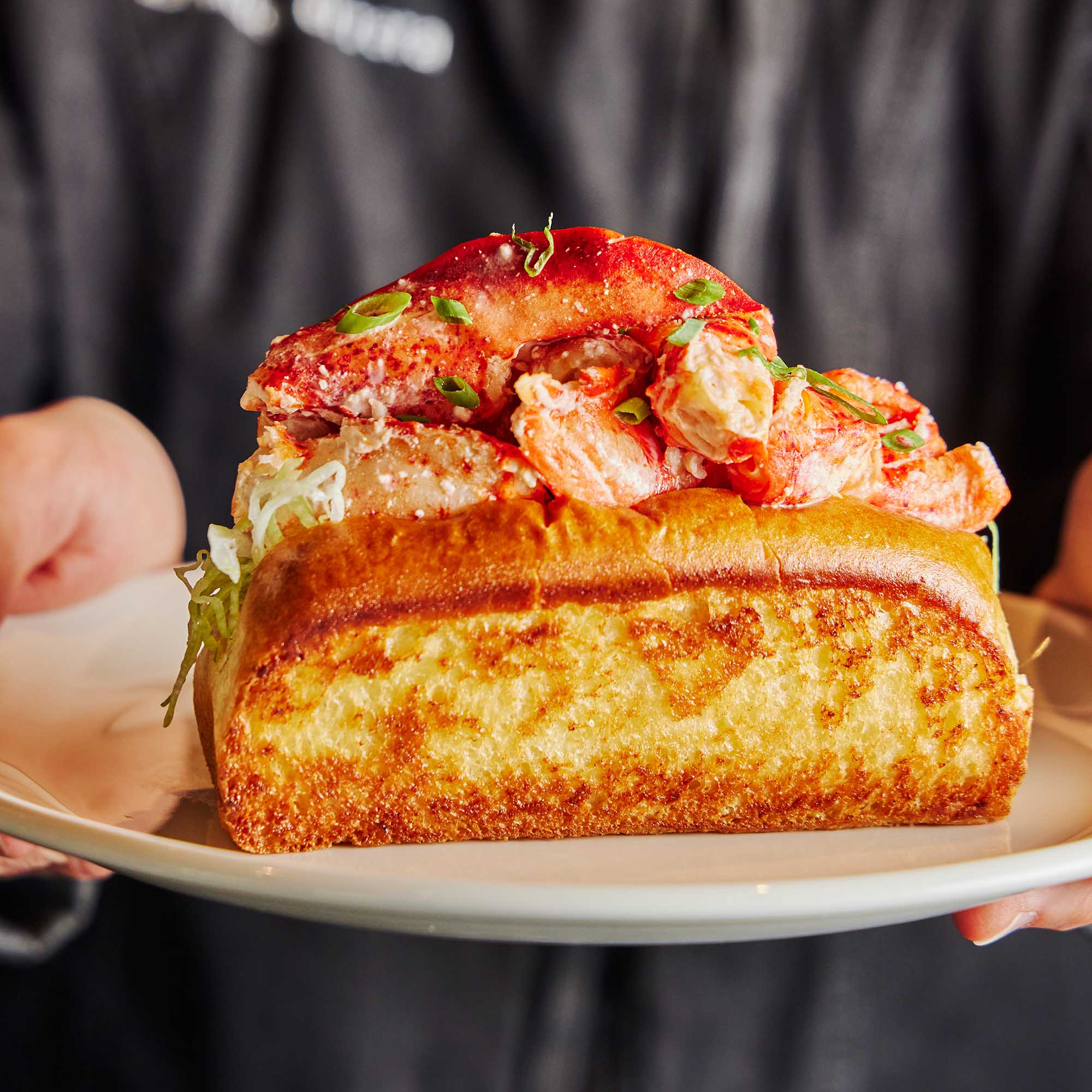 Chef holding a lobster roll on a plate.